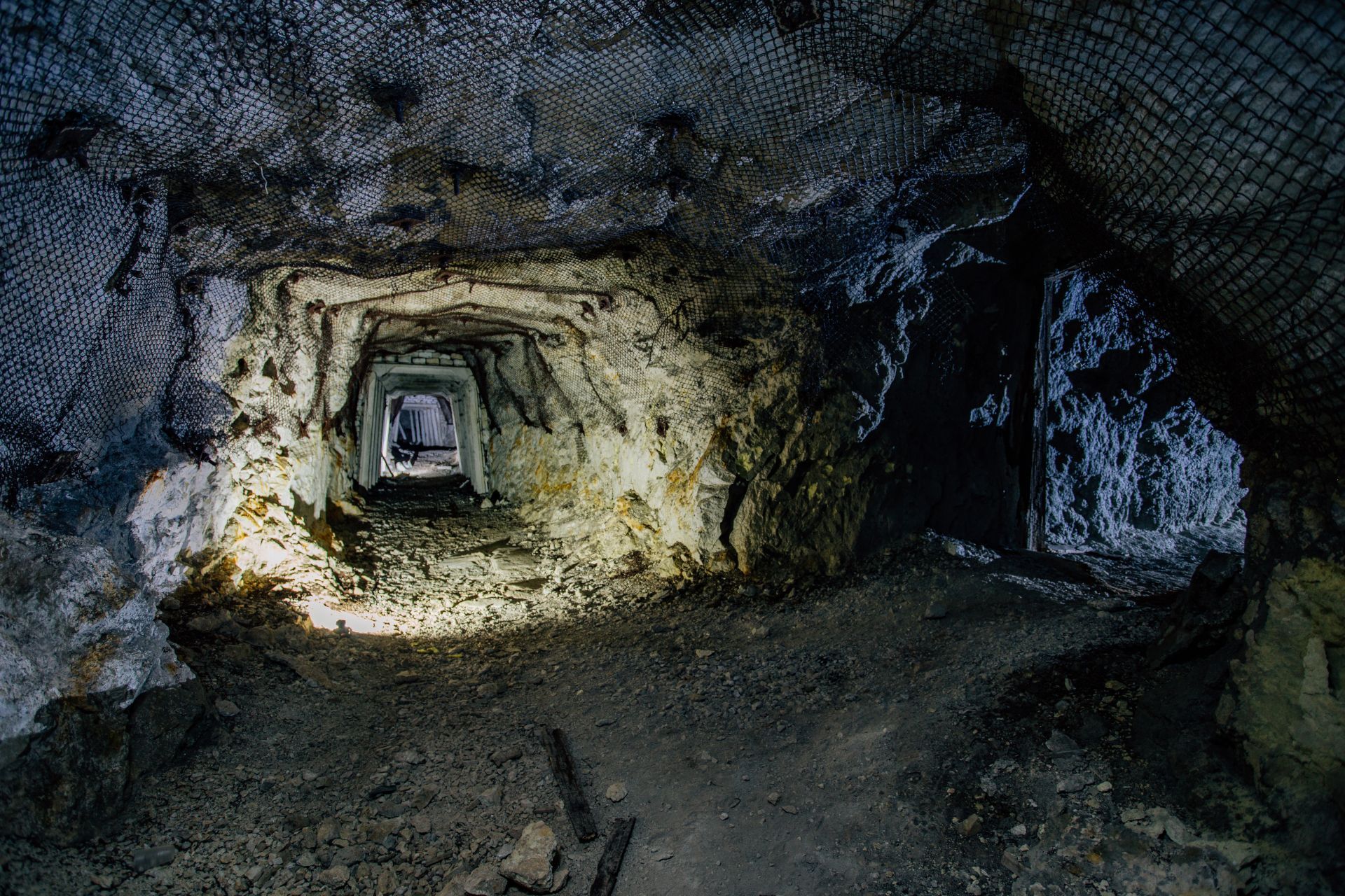 Inside a dim cave tunnel, a square opening recedes into the distance.