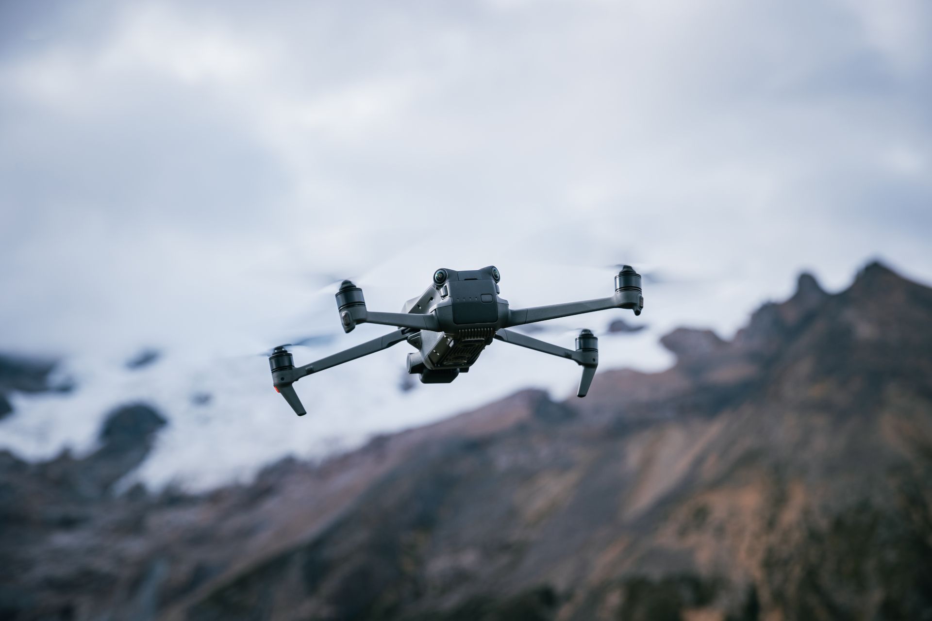 Drone flying in front of rocky mountains under a cloudy sky