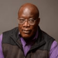 A man wearing glasses and a purple shirt is wearing a black vest.