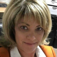 A woman with blonde hair and a white shirt is smiling for the camera.