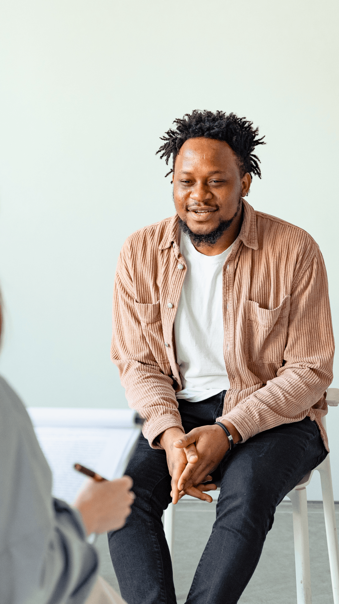 A man is sitting in a chair talking to another man.