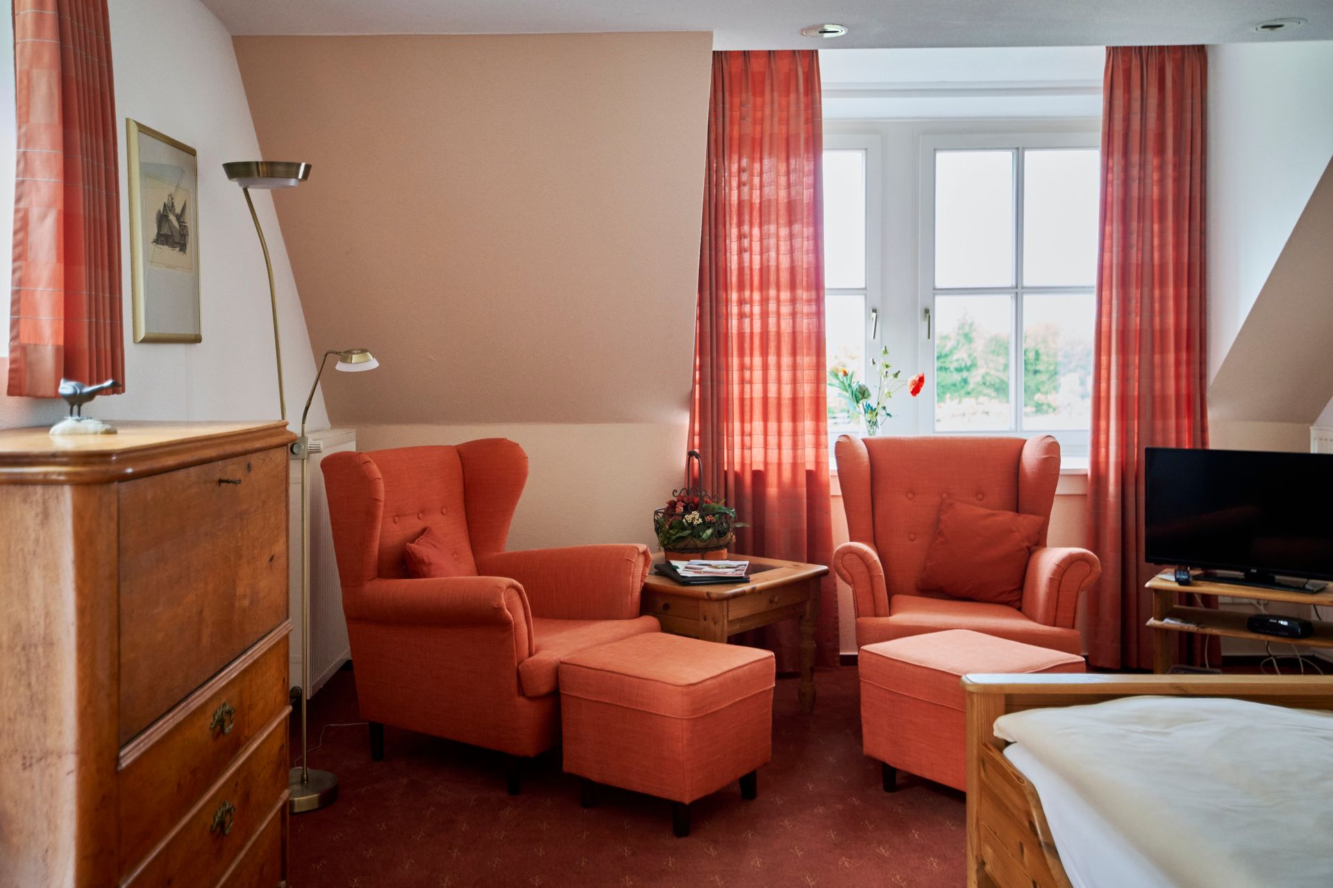 Ein Wohnzimmer mit einem Bett, Stühlen, Ottomanen und einem Fernseher.
