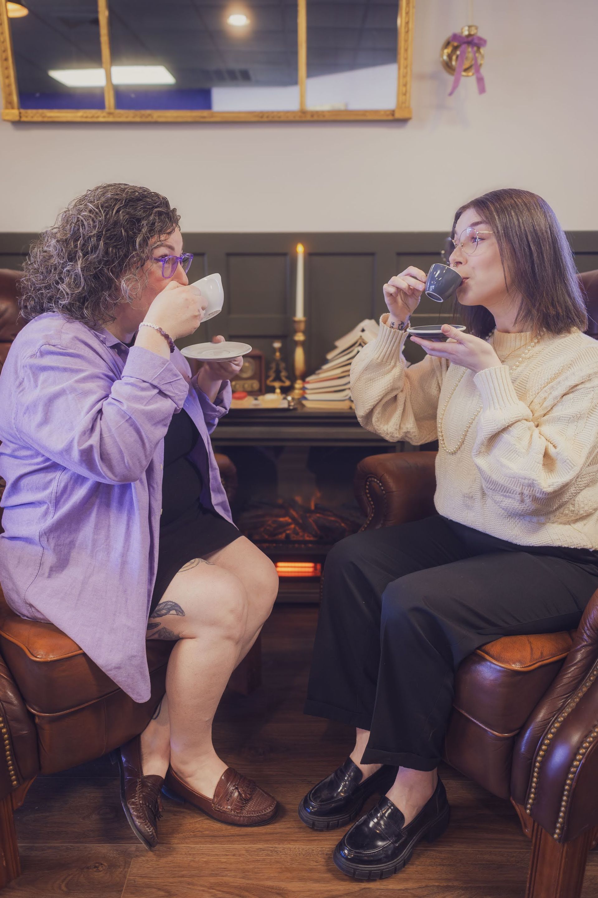two figures sipping from tea cups while looking at each other and sitting opposite of one another