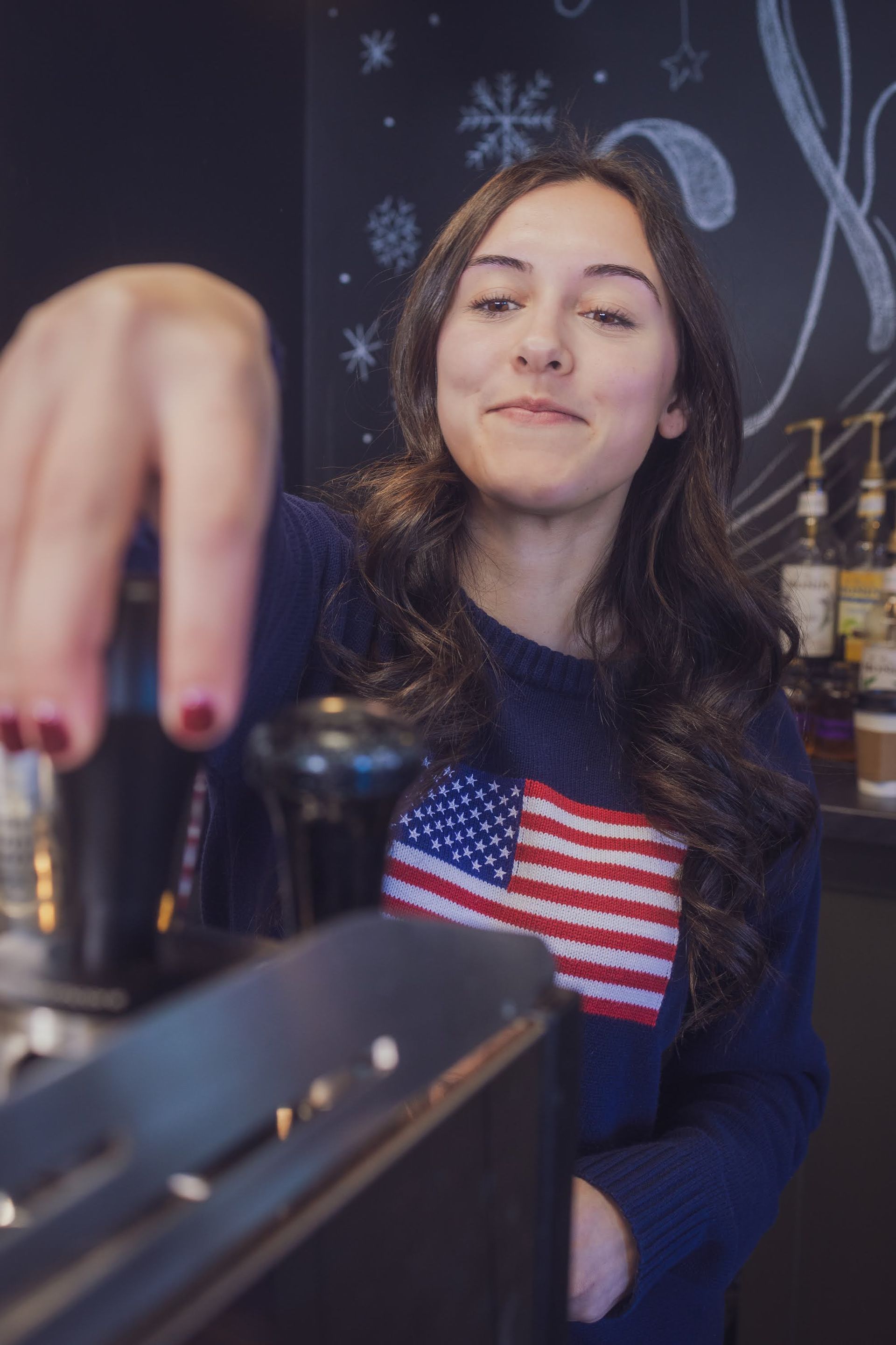 women reaching for item on top of an espresso machine