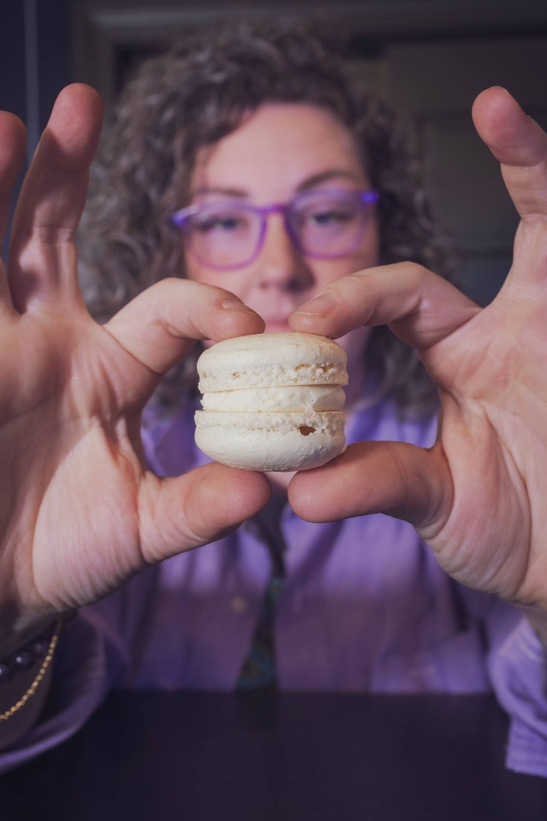 figure holding a white macaron using their index fingers on top and their thumbs below to hold the macaron