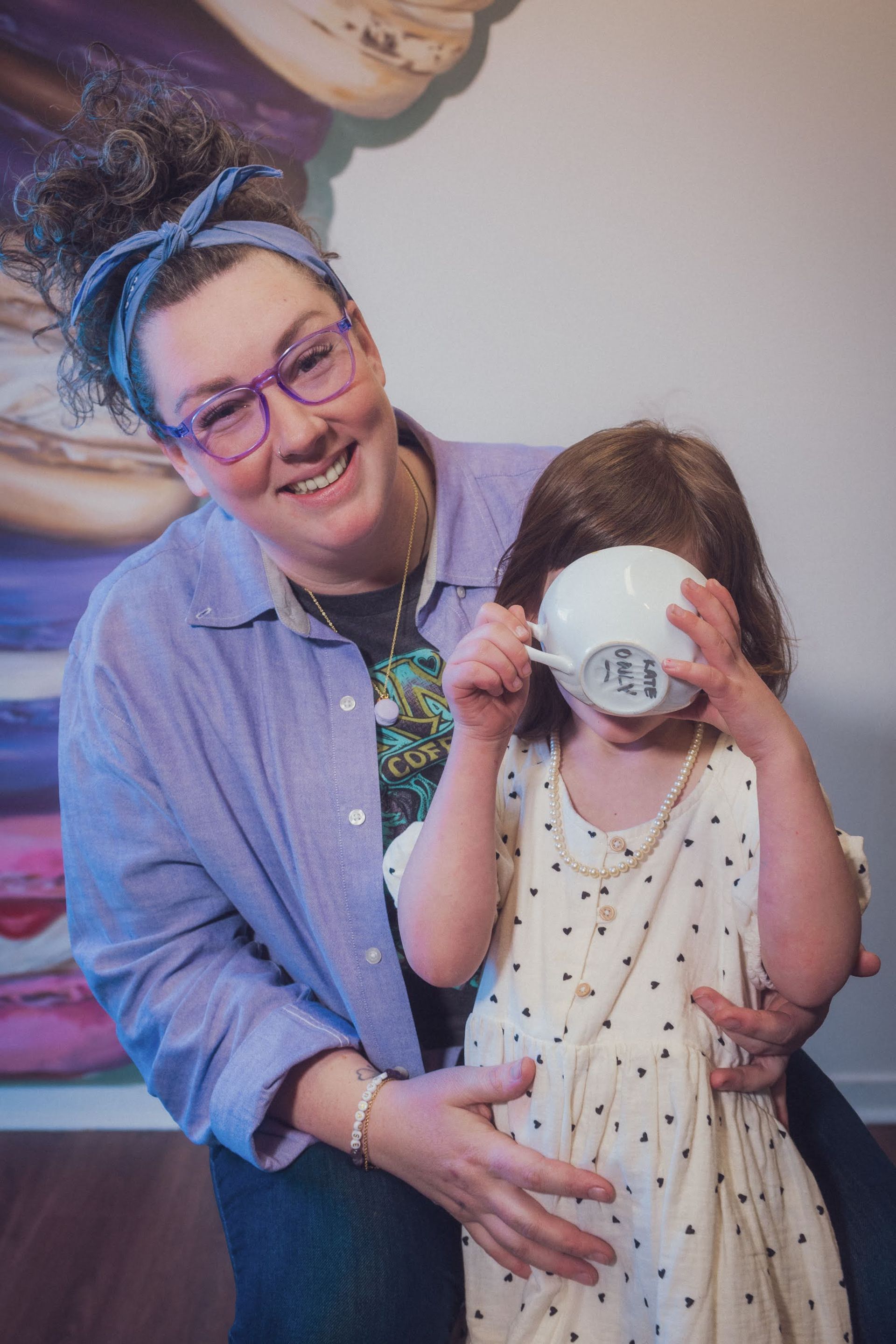 a women kneeling down behind a child figure drinking out of a white coffee cup blocking the view of their face
