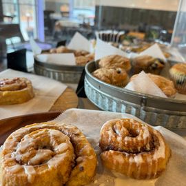 2 cinnamon buns with various pastries behind in pastry case