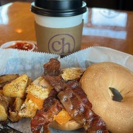 a breakfast sandwich on a bagel in the forefront with a hot coffee in the background