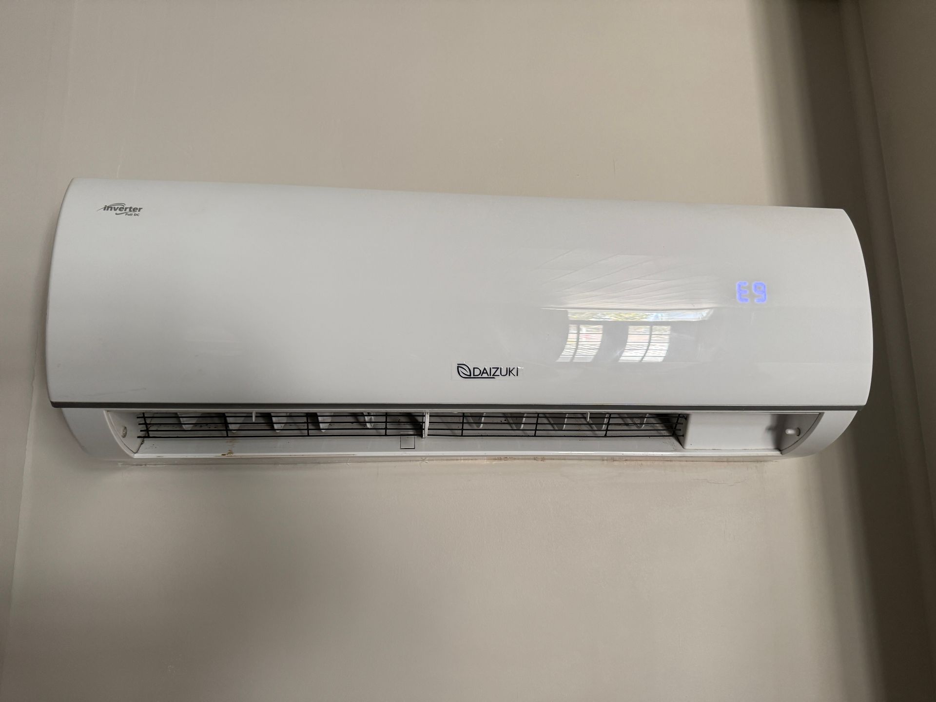 White wall-mounted air conditioner above a window with sheer curtains