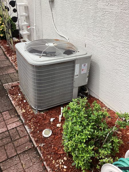 Technician installing an outdoor air conditioner unit on a white wall