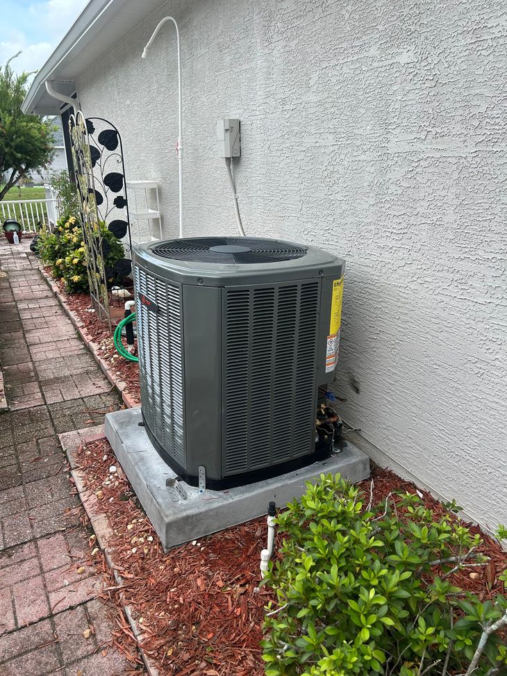 White air conditioner unit mounted below a window on a pink stucco wall.