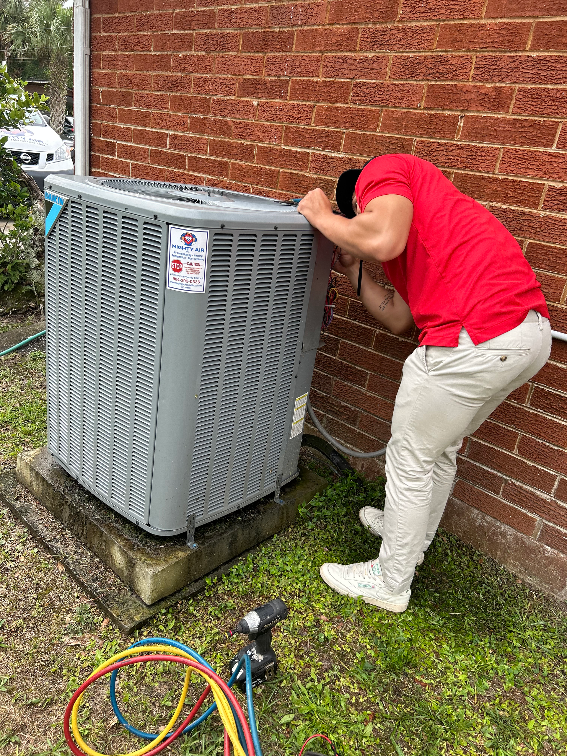 Outdoor wall-mounted air conditioner units beside a modern house and green hedge.
