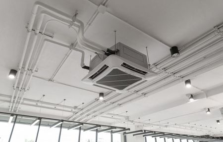 Ceiling-mounted HVAC unit and exposed pipes in a bright industrial interior
