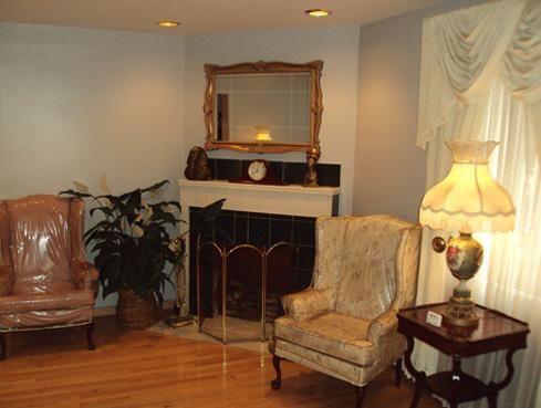 Elegant living room with fireplace, ornate chairs, lamp, and framed mirror on mantel