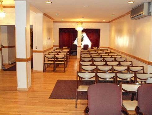 Empty meeting room with rows of chairs facing red curtains and a podium at the back