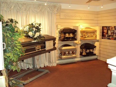 Funeral showroom with multiple caskets on display, draped curtains, and floral arrangements