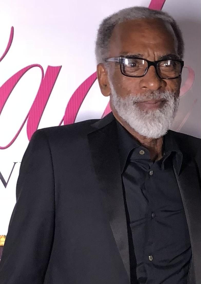 Man in dark suit and glasses posing before a white and pink backdrop