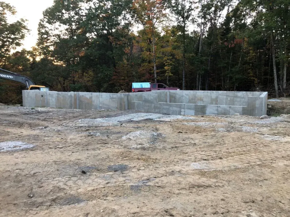 A concrete wall is being built in a dirt field with trees in the background.