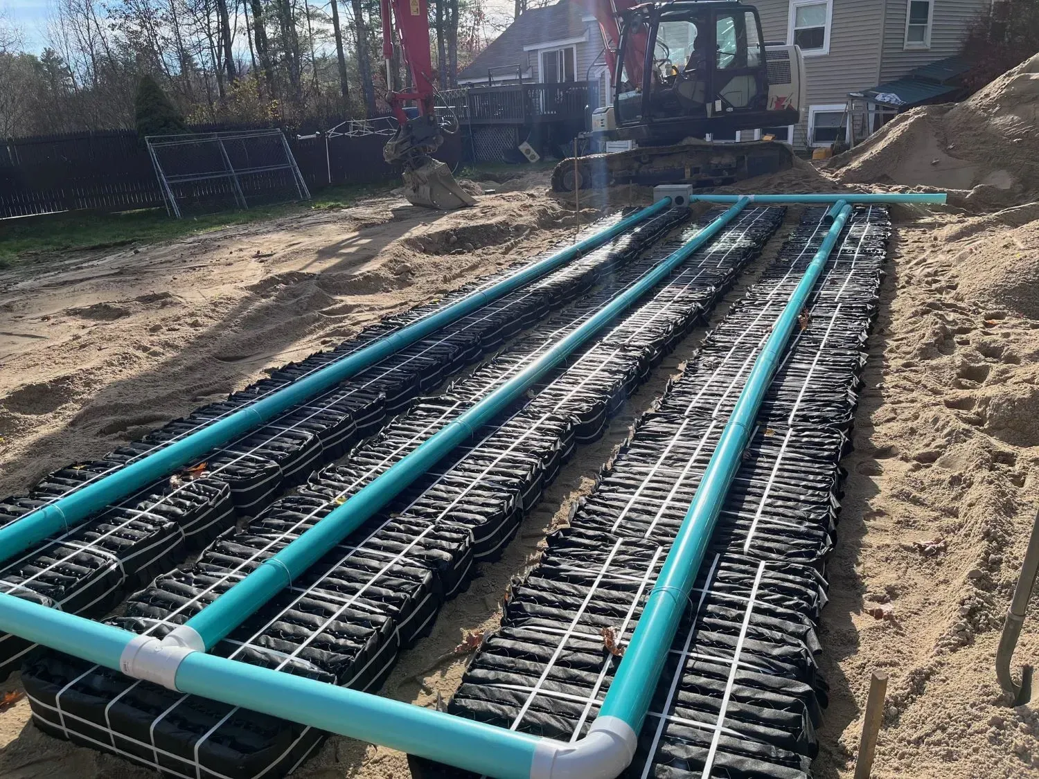 Blue pipes laid over black rebar on a construction site, with an excavator in the background.