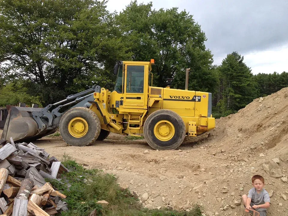 A boy sits in front of a yellow volvo bulldozer
