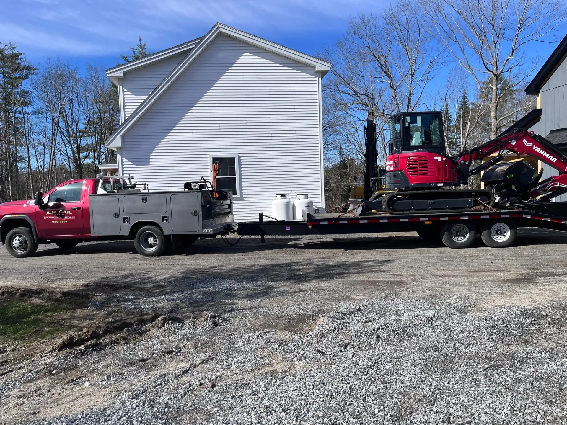 A red truck is towing a red excavator on a trailer.