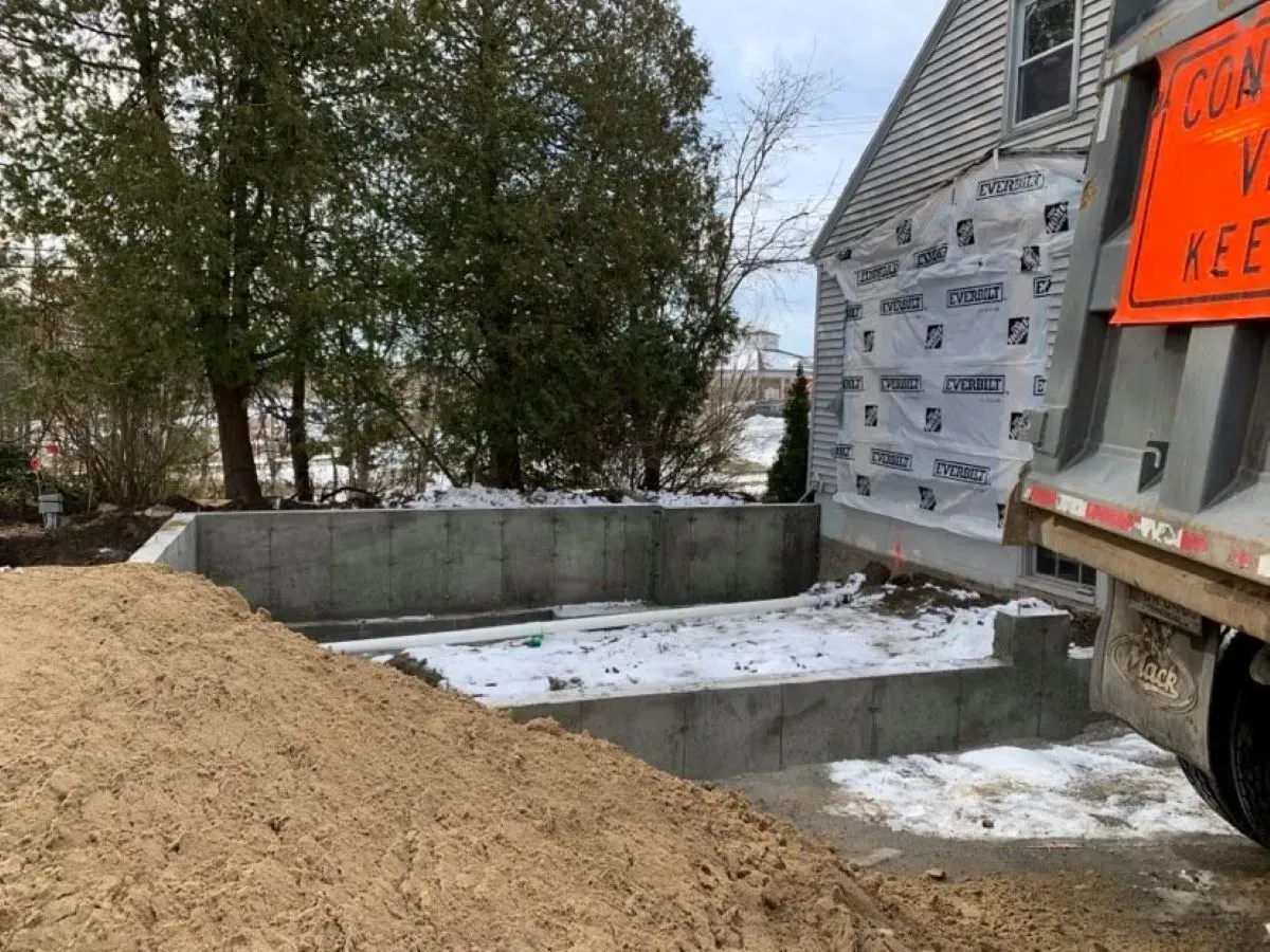 A dump truck is parked in front of a house under construction.