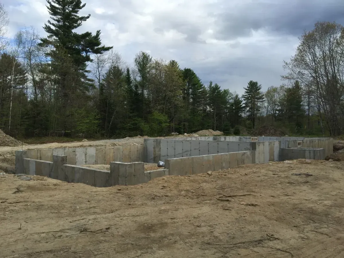 A concrete foundation is being built in a dirt field with trees in the background