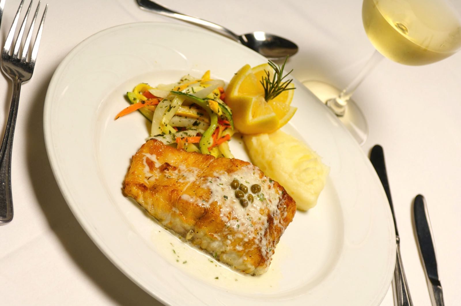 Grilled salmon filet served with vegetables and a lemon garnish, photographed with bright, clean fine-dining presentation.