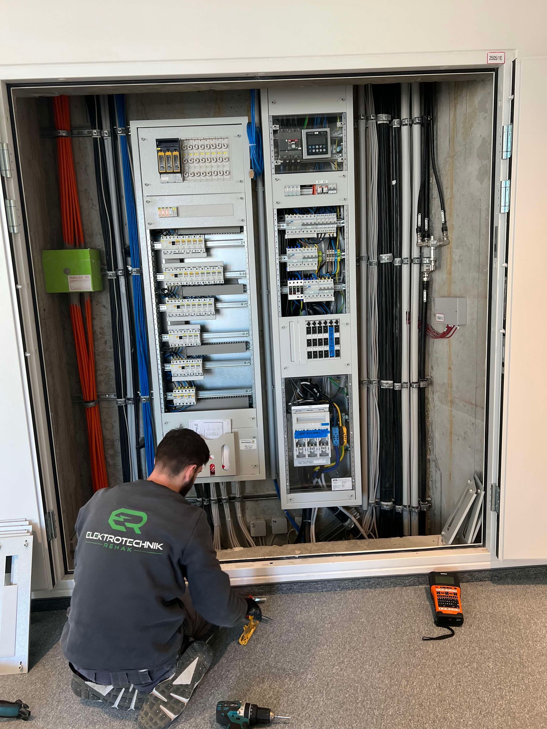 Ein Techniker kniet vor einem offenen Elektroschrank und arbeitet an der Verkabelung in einem Hauswirtschaftsraum.