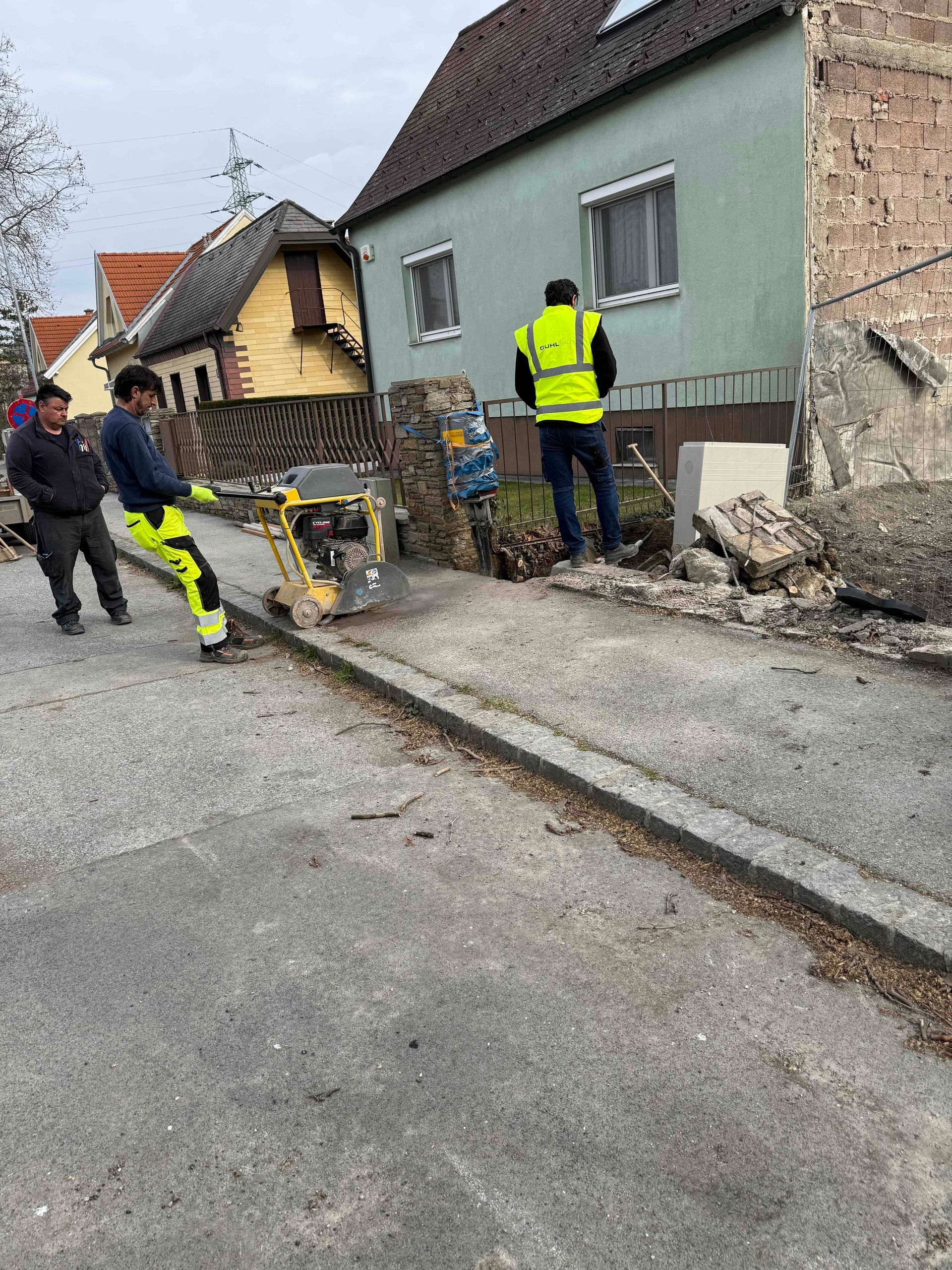 Arbeiter brechen mit einem Presslufthammer einen Gehweg neben einem Haus in einer Wohnstraße auf.