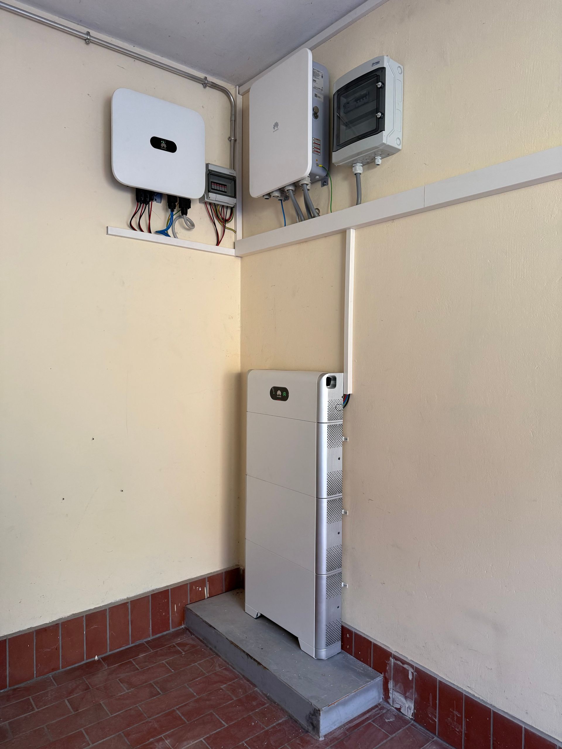 Elektroschränke und Schalttafel in einer Technikecke mit beigefarbenen Wänden und roten Fliesen.