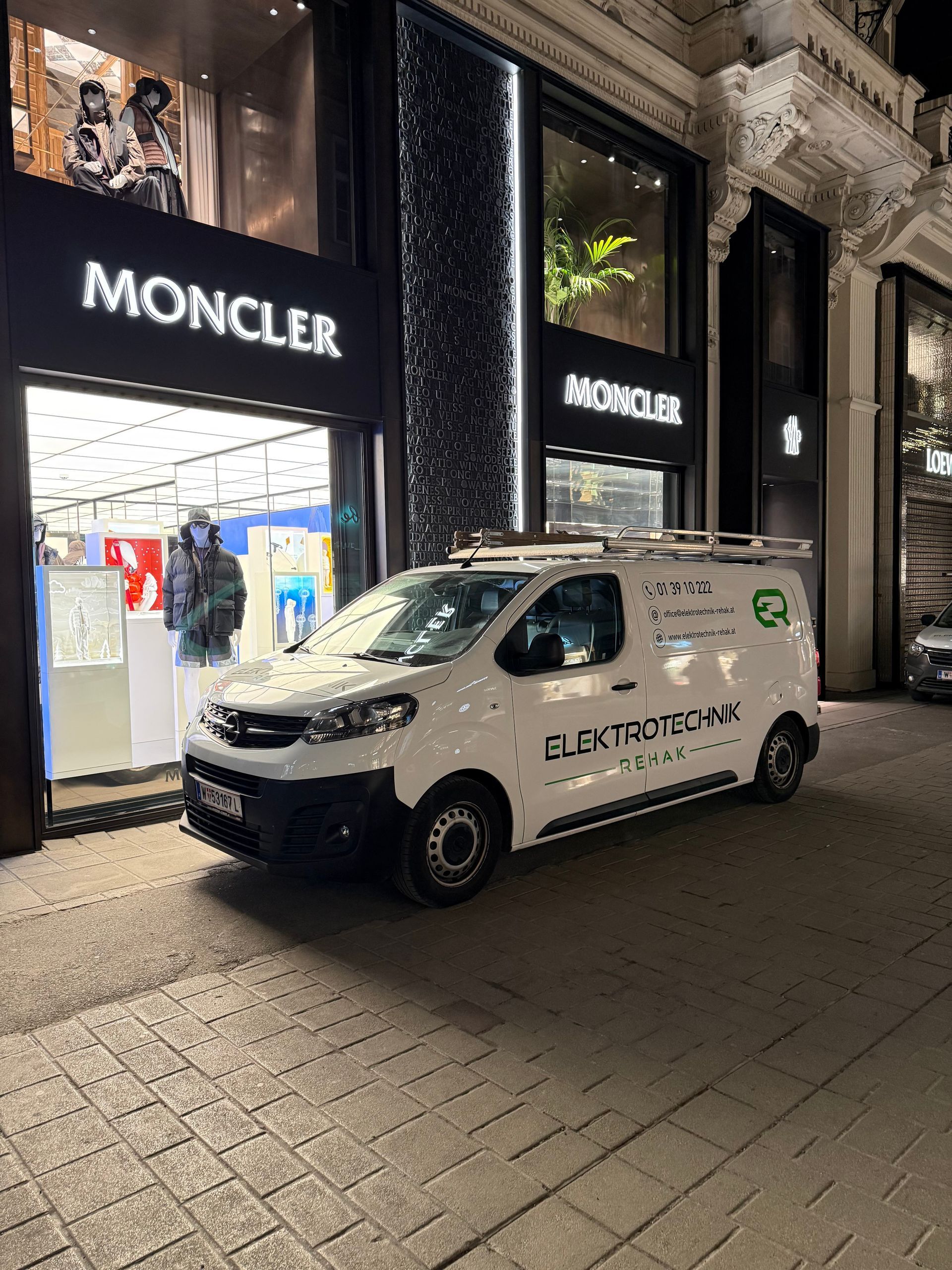 Ein weißer Citroën-Lieferwagen parkt nachts vor einem Moncler-Geschäft in einer Straße der Stadt.