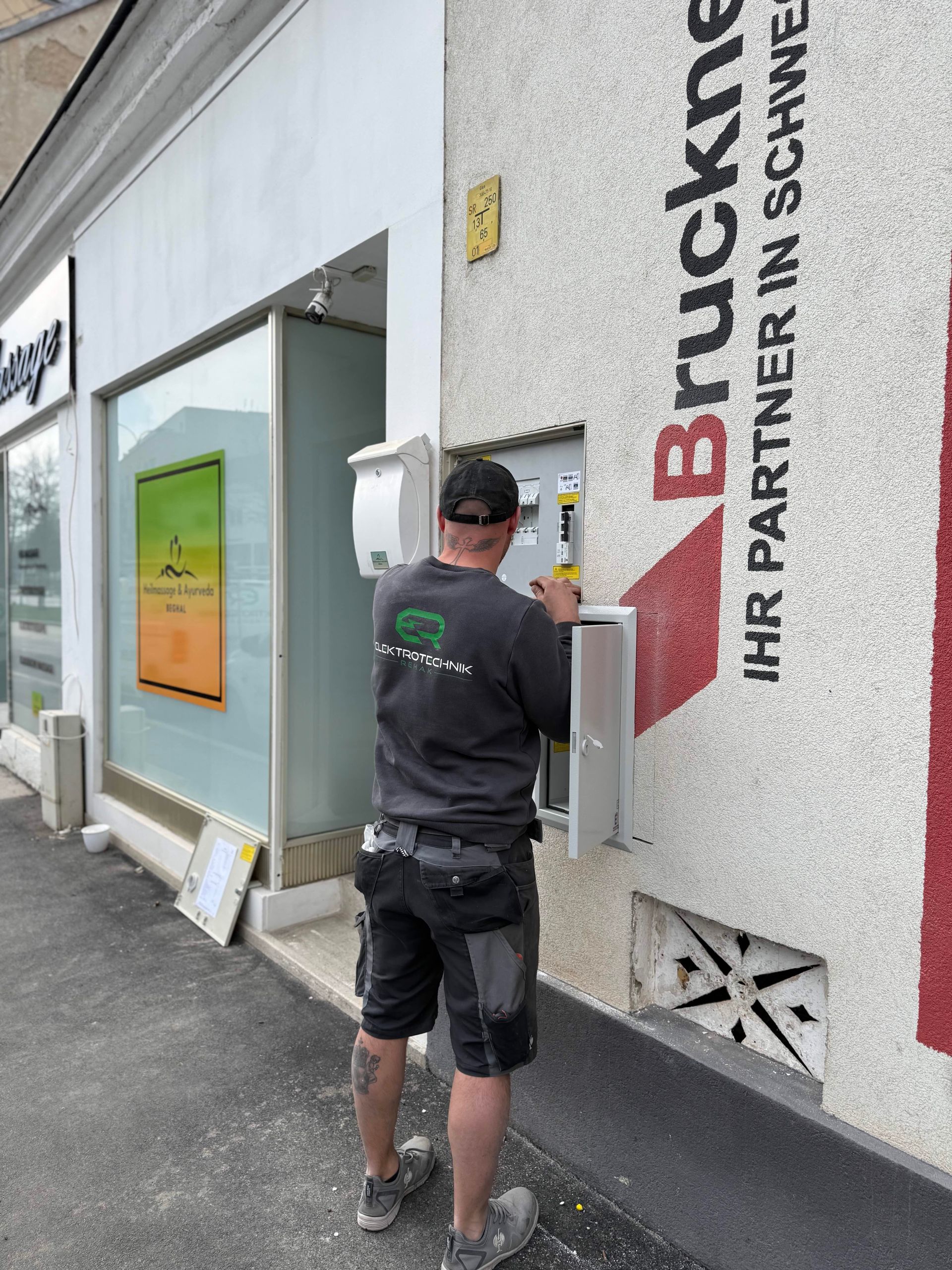 Ein Arbeiter bringt rote Buchstaben an einer Gebäudewand vor einem Optikergeschäft an.