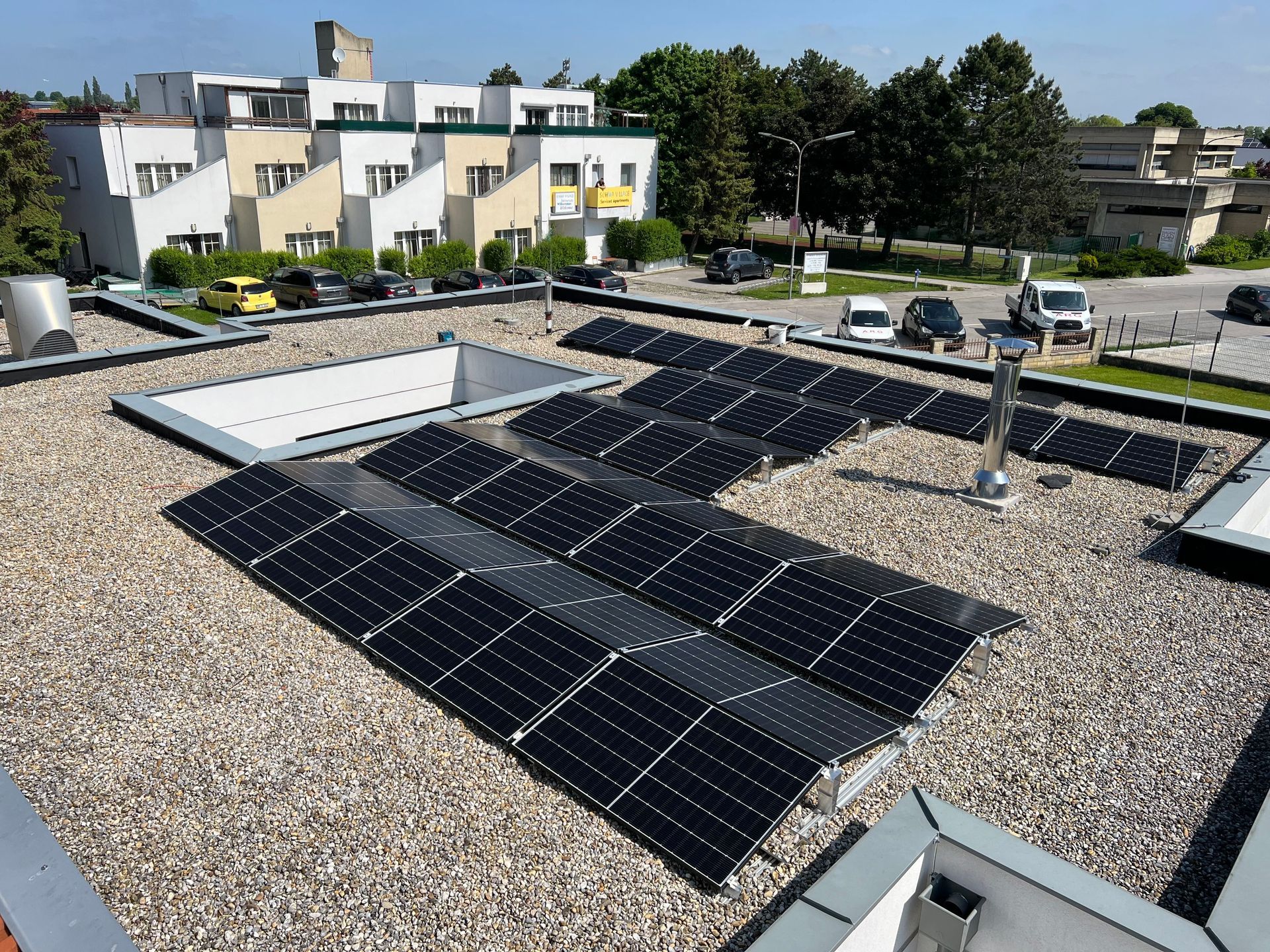 Solarpaneele auf einem mit Kies bedeckten Flachdach neben Wohnhäusern und Bäumen