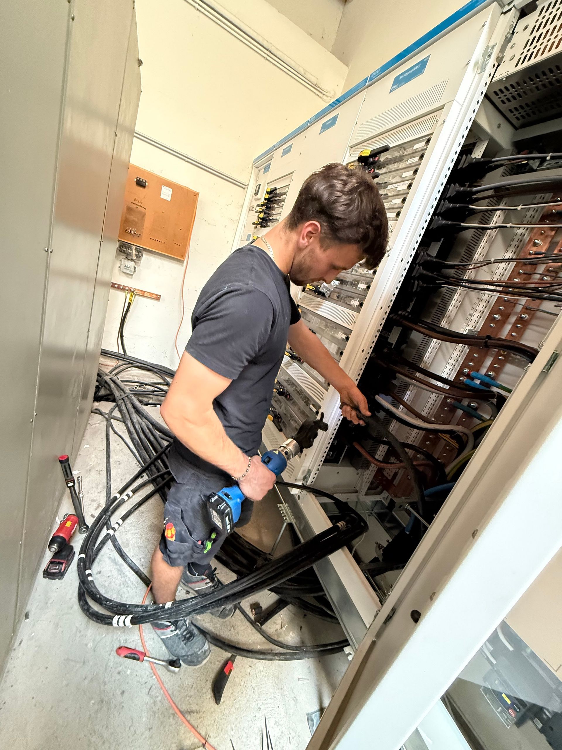 Techniker arbeitet in einem Elektroschrank und hantiert mit Verkabelungen und Kabeln in einem Serverraum.
