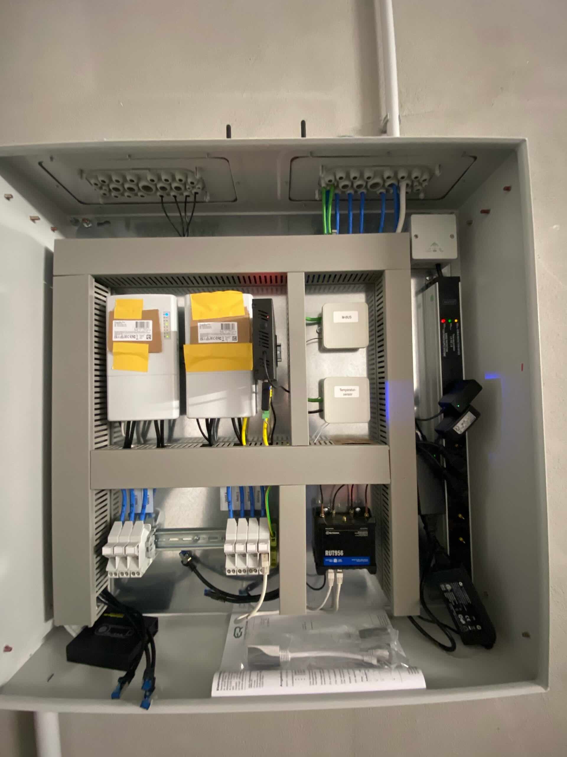 Offener elektrischer Schaltschrank mit Kabeln, Relais und Schaltungskomponenten in einem grauen Metallgehäuse