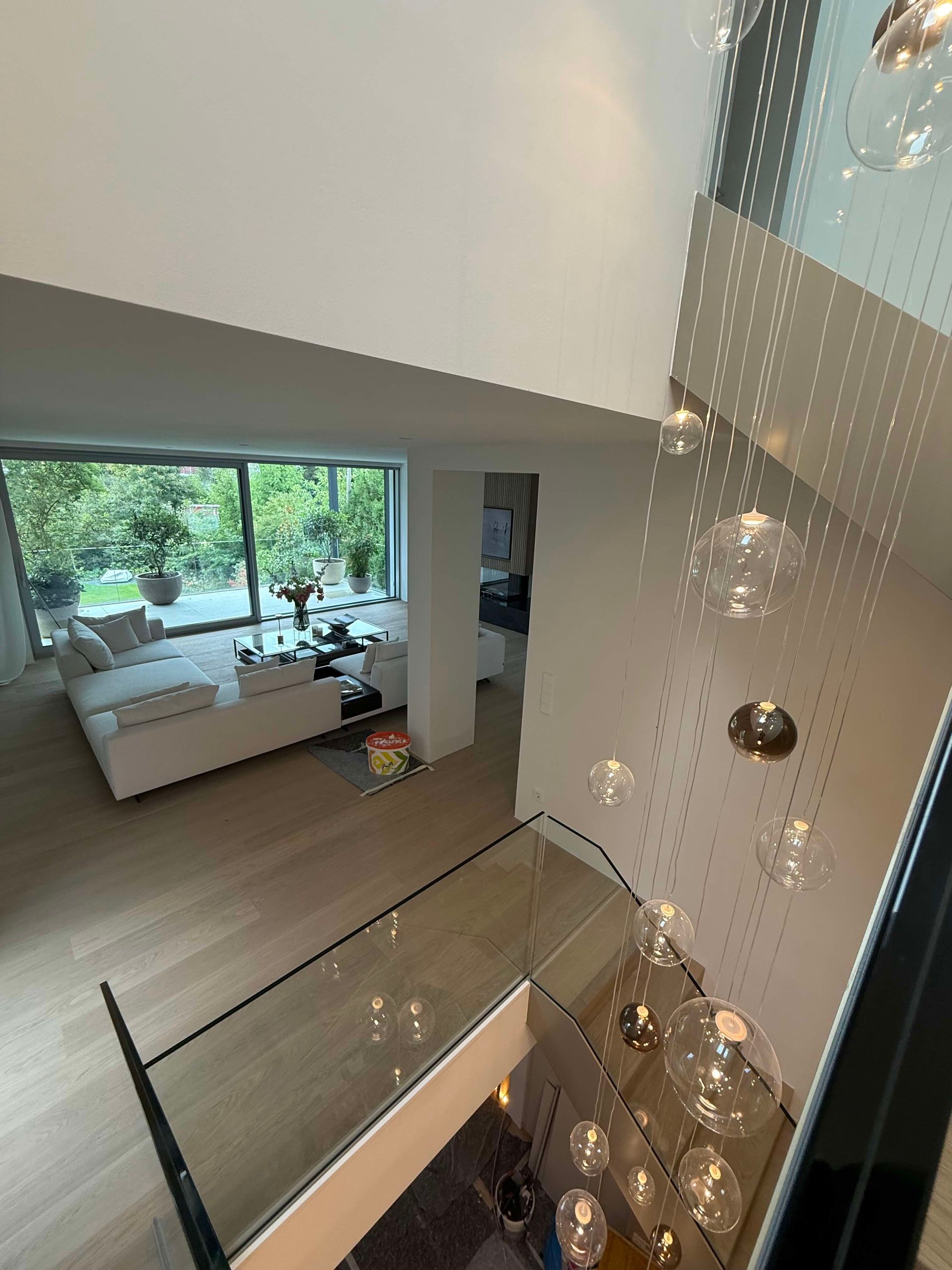 Moderne Atriumtreppe mit Blick auf ein helles Wohnzimmer mit großen Fenstern und einem weißen Sofa