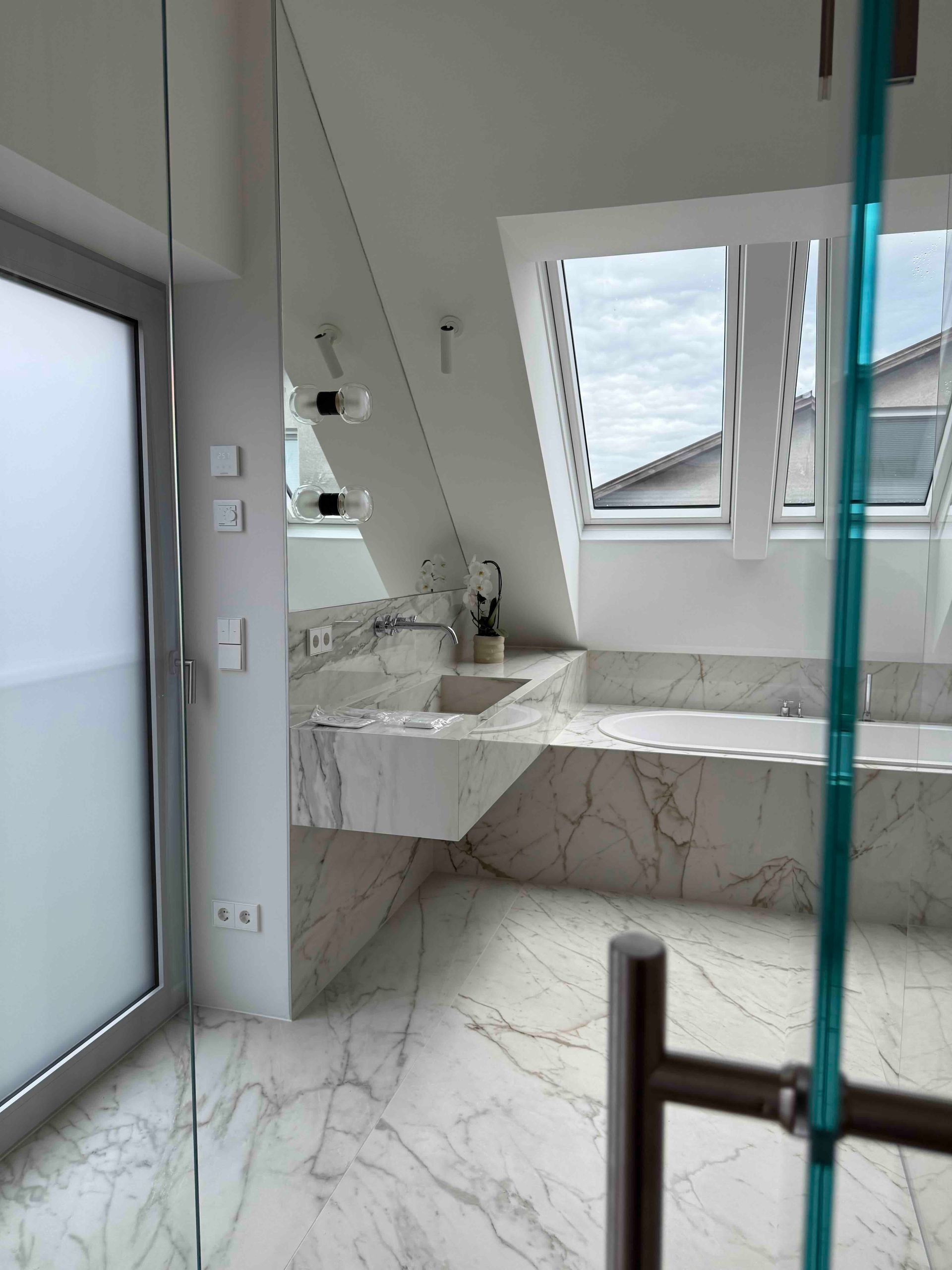 Modernes Badezimmer mit Marmorfliesen, eingebauter Badewanne und großen Fenstern an einer Dachschräge