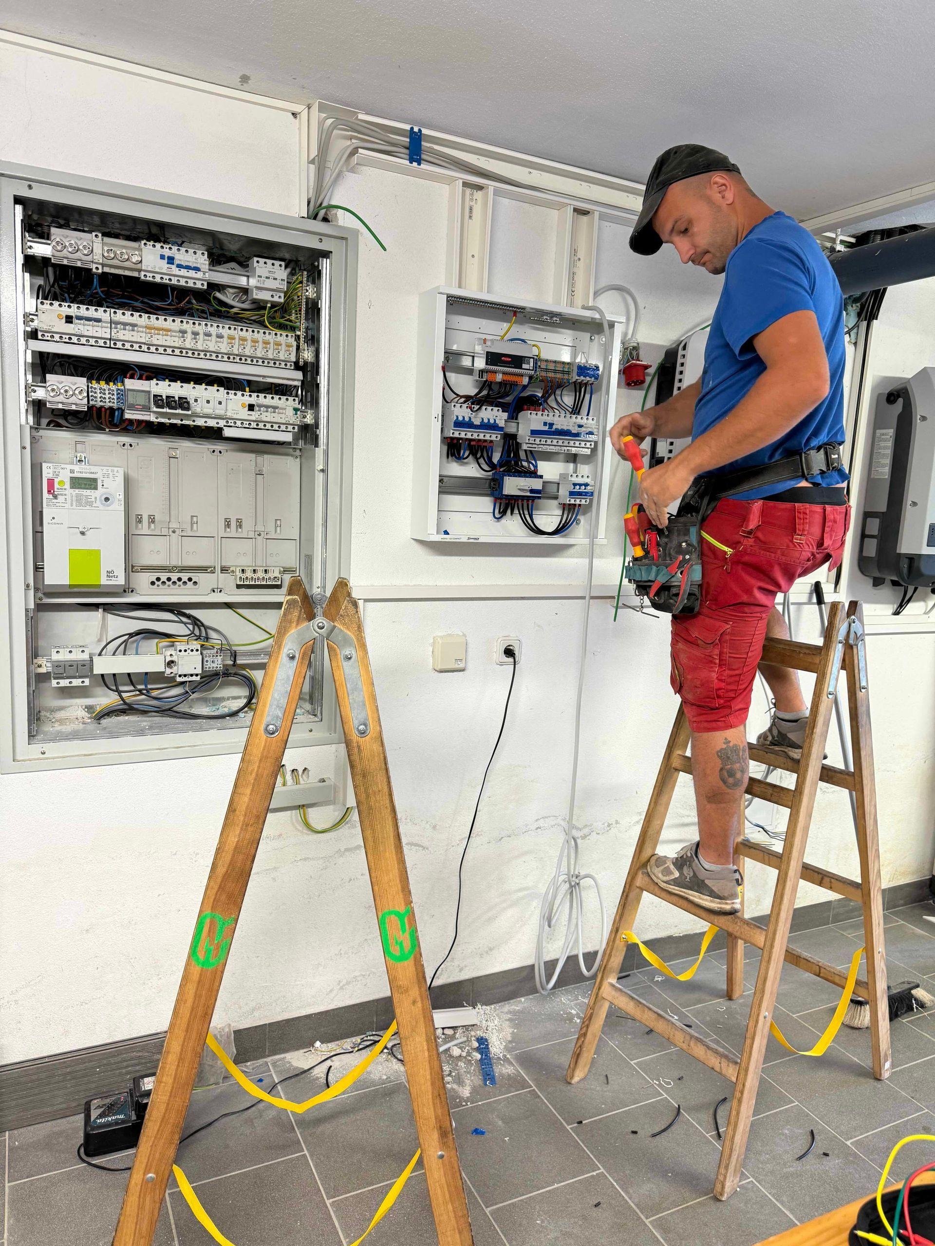 Ein Elektriker arbeitet in einem Innenraum an freiliegenden, an der Wand montierten Schaltschränken