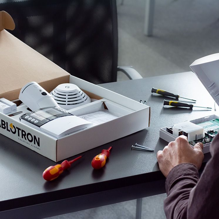 Hände montieren ein BLUTRON-Gerät auf einem Schreibtisch, in dessen Nähe sich Werkzeuge und rote Schraubendreher befinden.