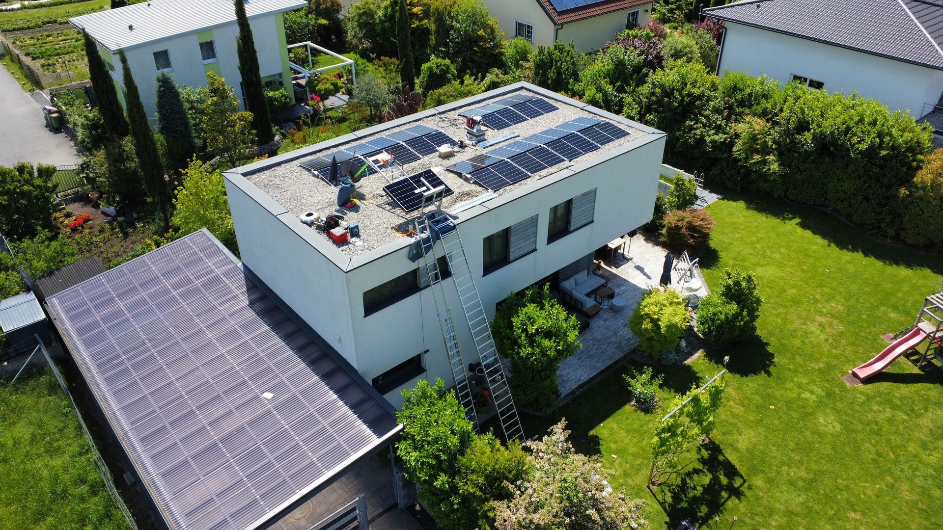Luftaufnahme eines weißen Hauses mit Solarpaneelen und einem angrenzenden Garten.