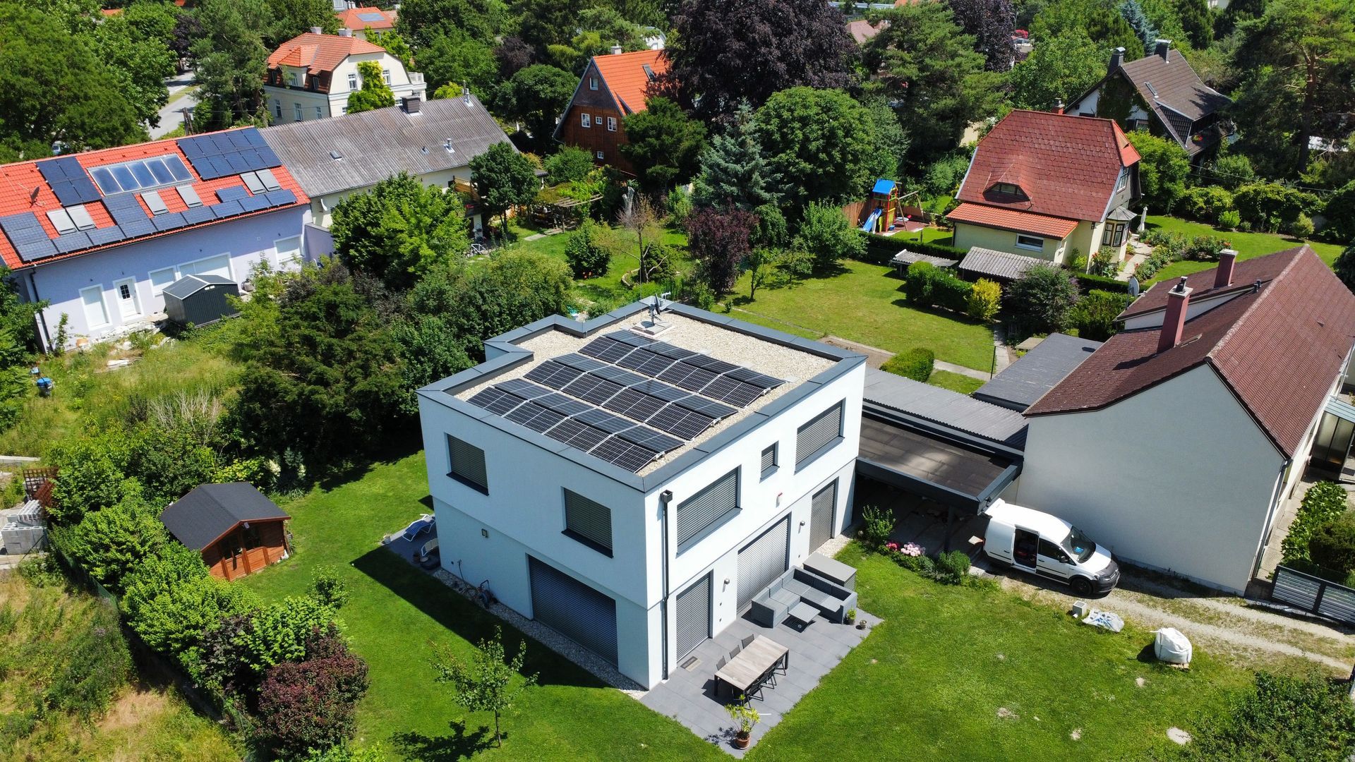Luftaufnahme eines modernen weißen Hauses mit Solarpaneelen in einer grünen Vorstadtsiedlung