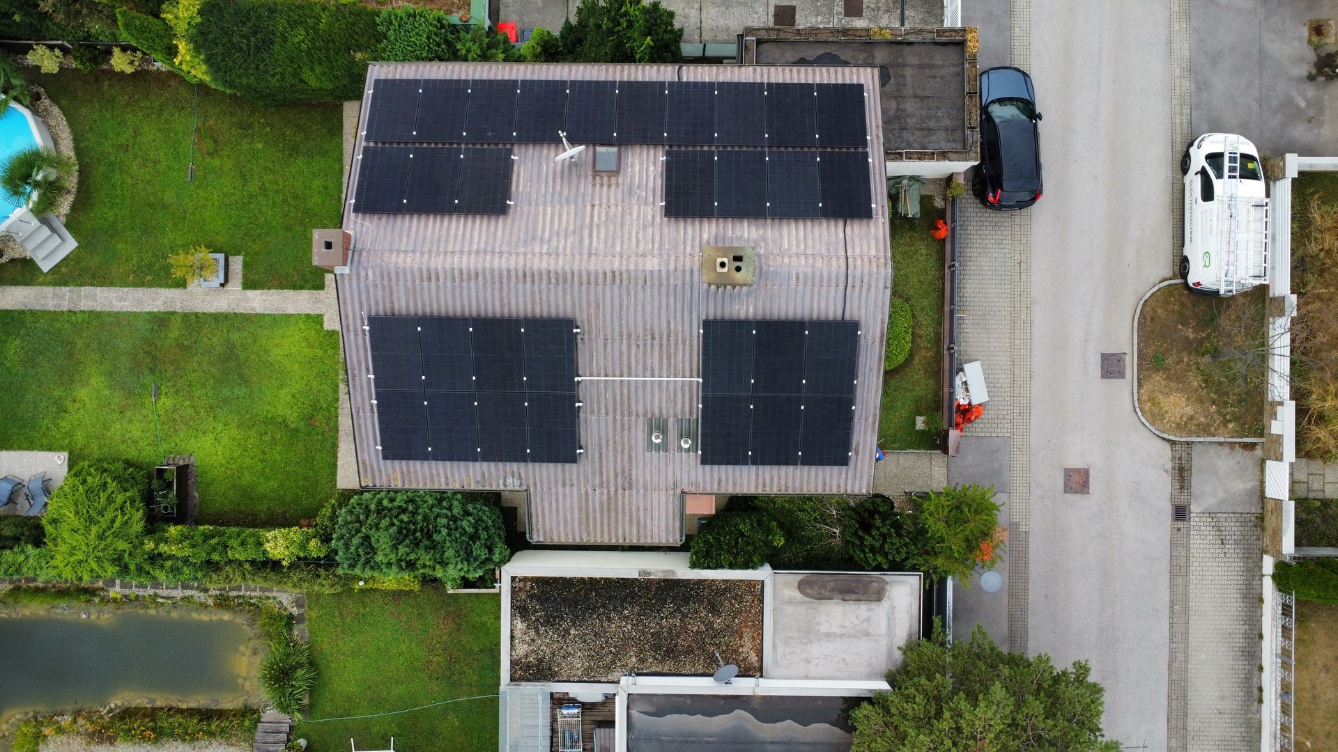 Luftaufnahme eines Hauses mit Solarpaneelen auf dem Dach neben einer Wohnstraße