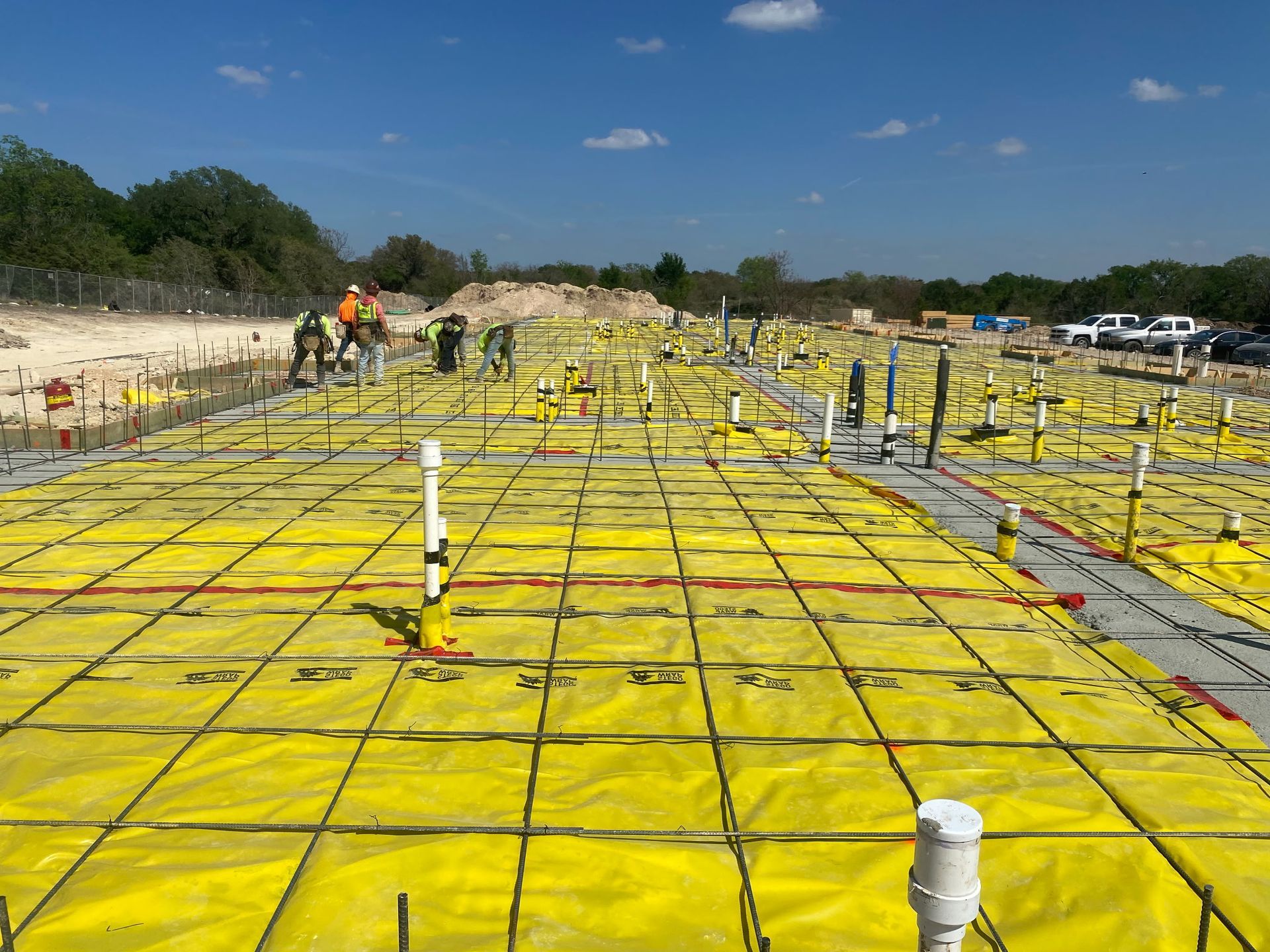 Construction site with yellow waterproofing membrane and rebar grid over a foundation slab