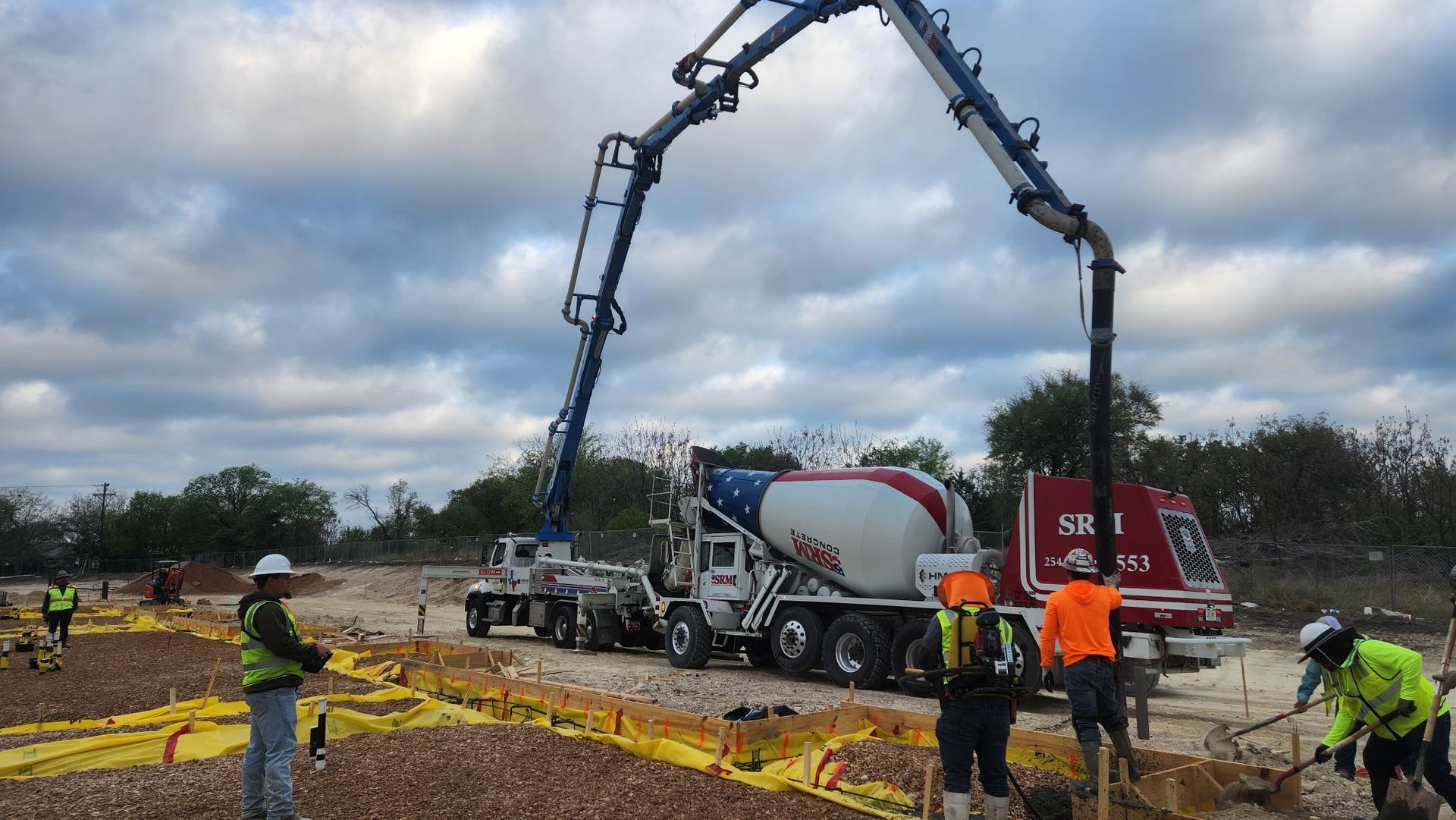 Construction site with concrete truck and pump boom arching overhead as workers guide the pour.