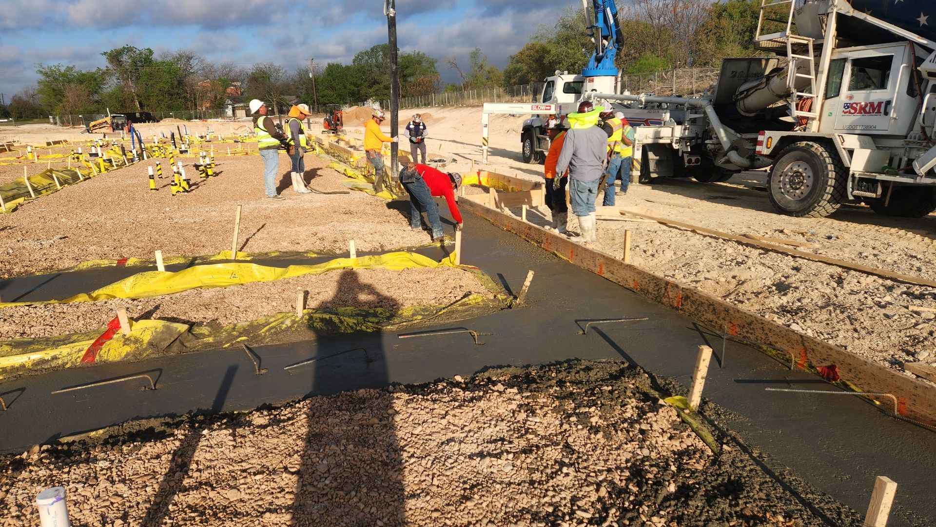 Workers repair a sidewalk and street with heavy machinery beside yellow caution tape and gravel.