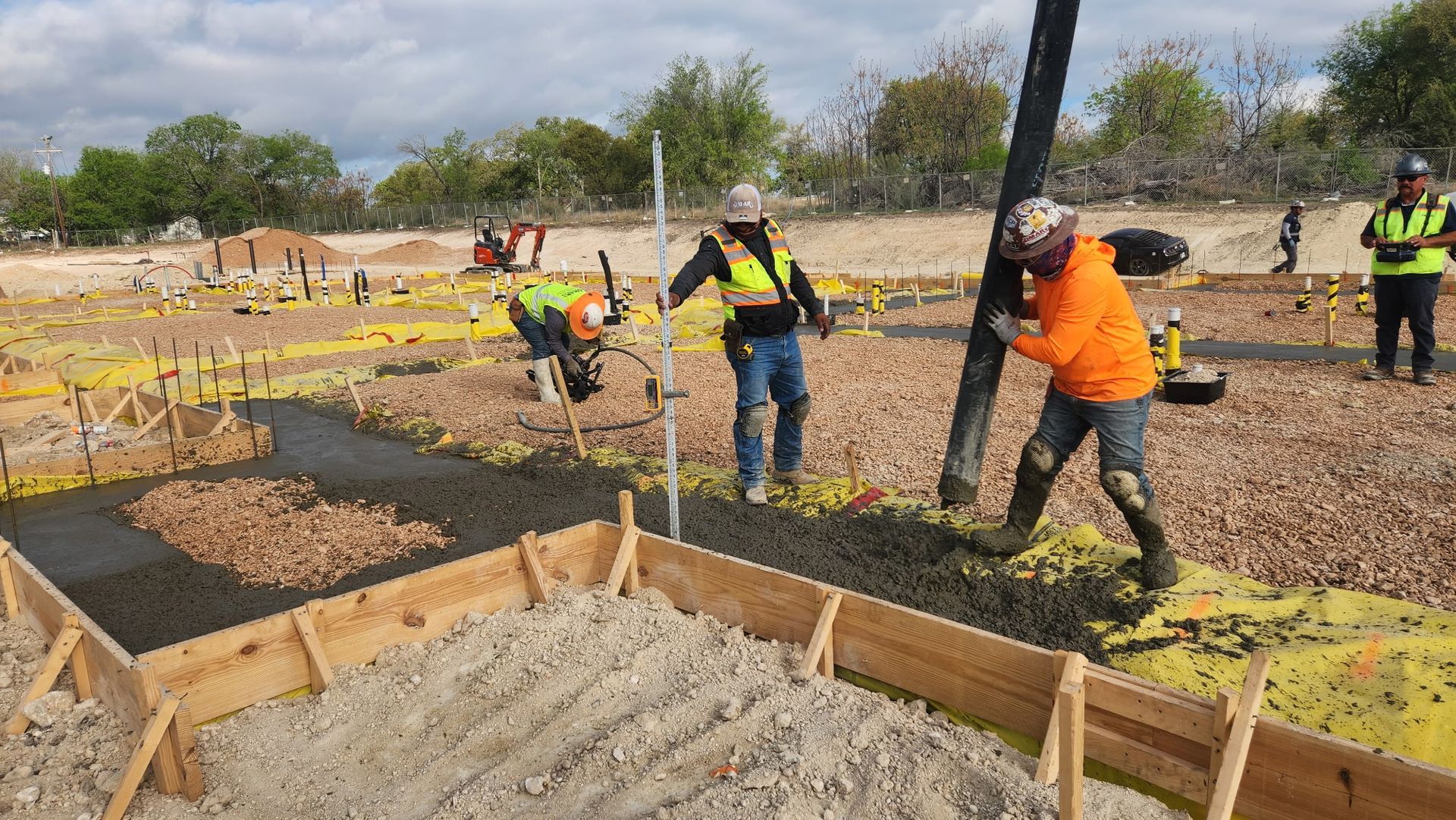 Workers pouring and leveling concrete for foundation footings at a construction site