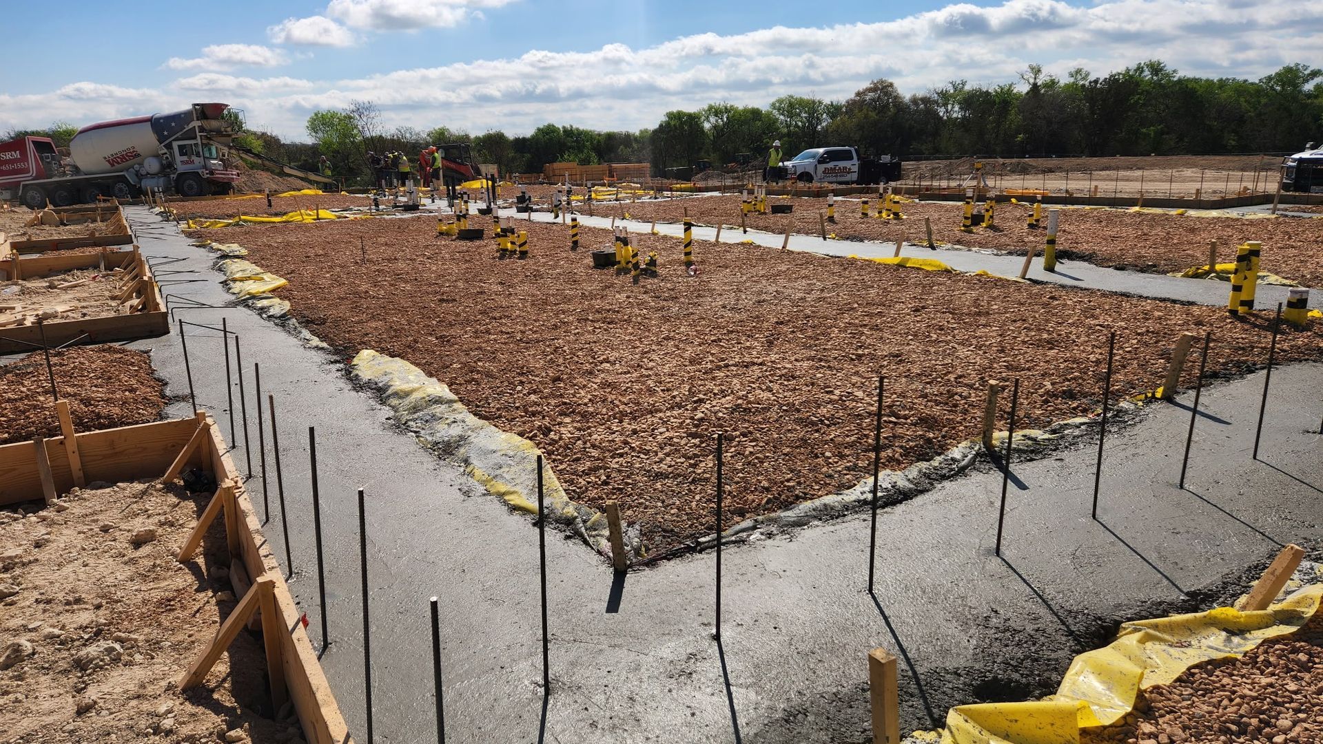 Concrete foundation slab under construction on a building site, with wooden forms and rebar in the foreground.