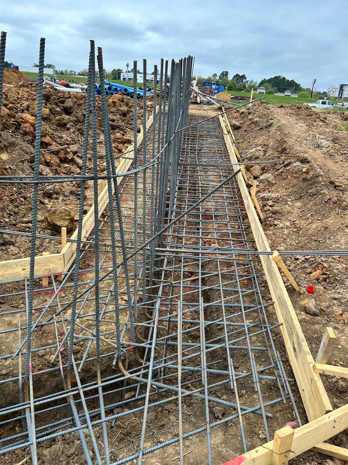 Steel rebar framework in a trench at a construction site, with dirt slopes and wooden supports.
