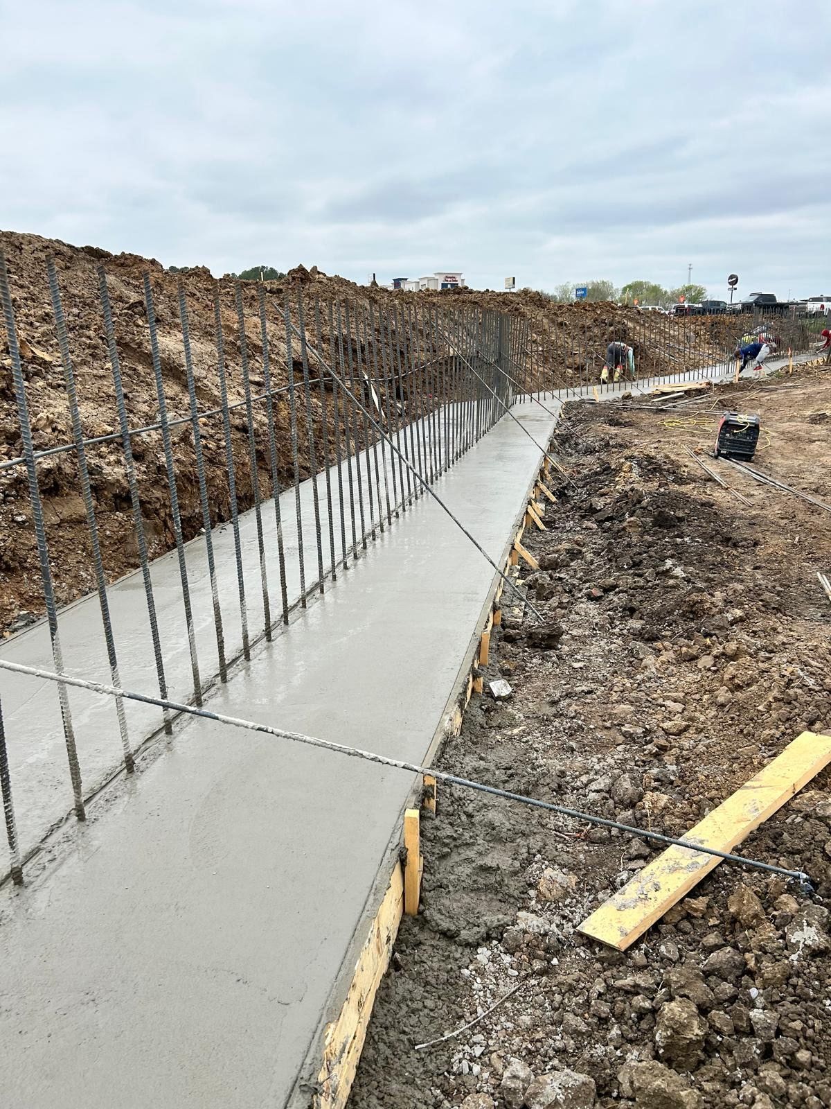 Concrete foundation trench with rebar forming a narrow walkway along a dirt construction site